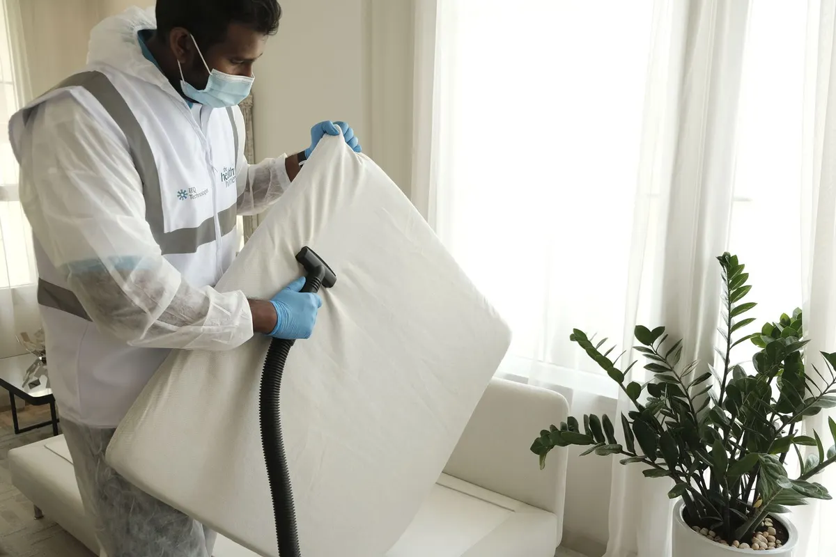 Profissional com equipamento de proteção higienizando colchão com aspirador
